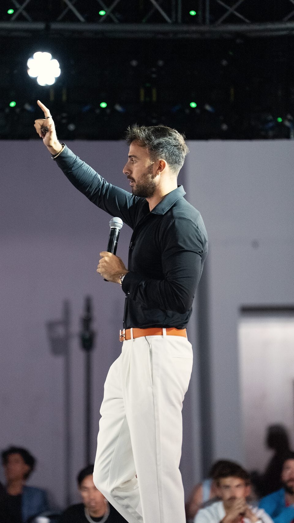 Marczell Klein on stage, pointing up as he speaks to the room.