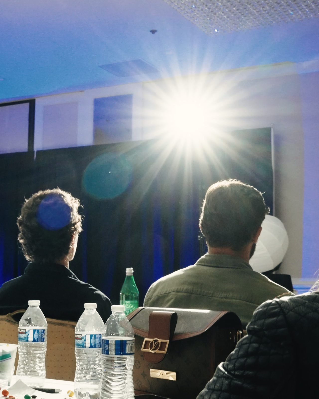 The back of a seminar audience, silhouetted against a bright stage light.