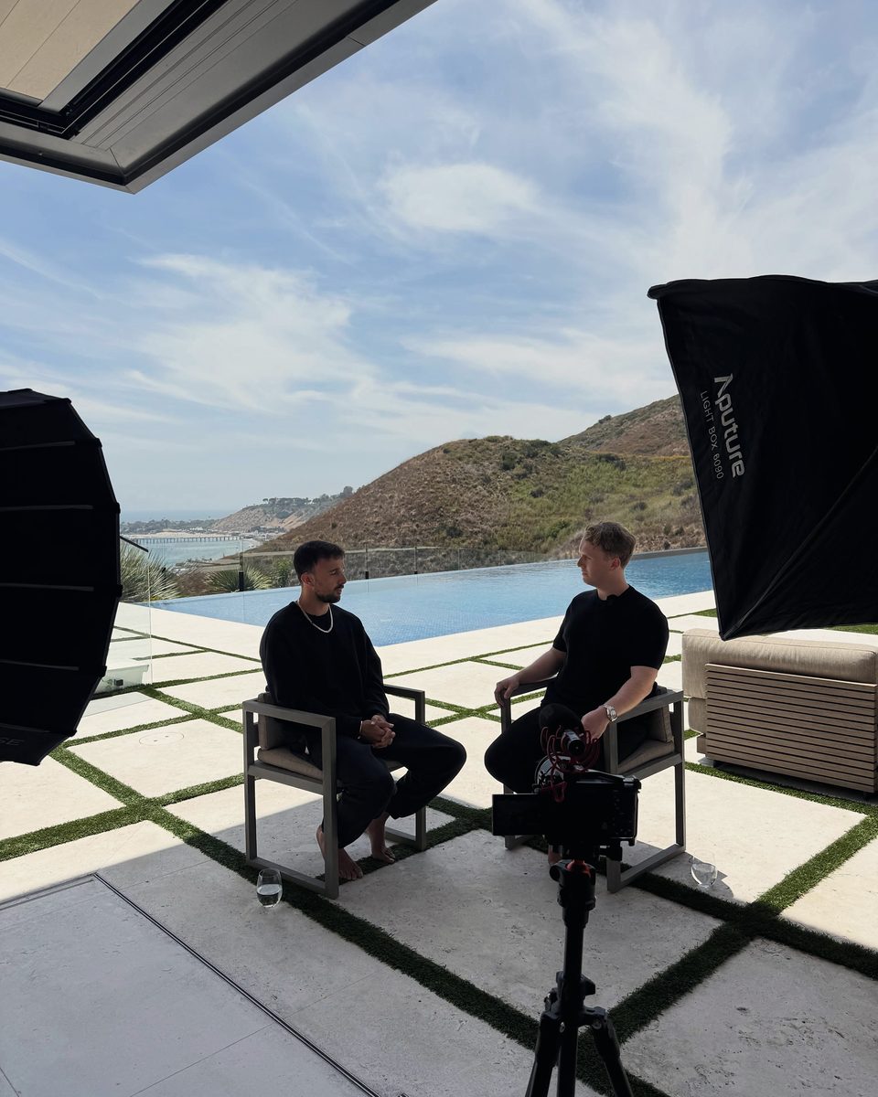 Marczell Klein in conversation with a guest on a terrace, a camera set up between them.