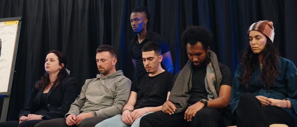 Volunteers seated in a row on stage, most with their eyes closed, during a hypnosis demonstration.