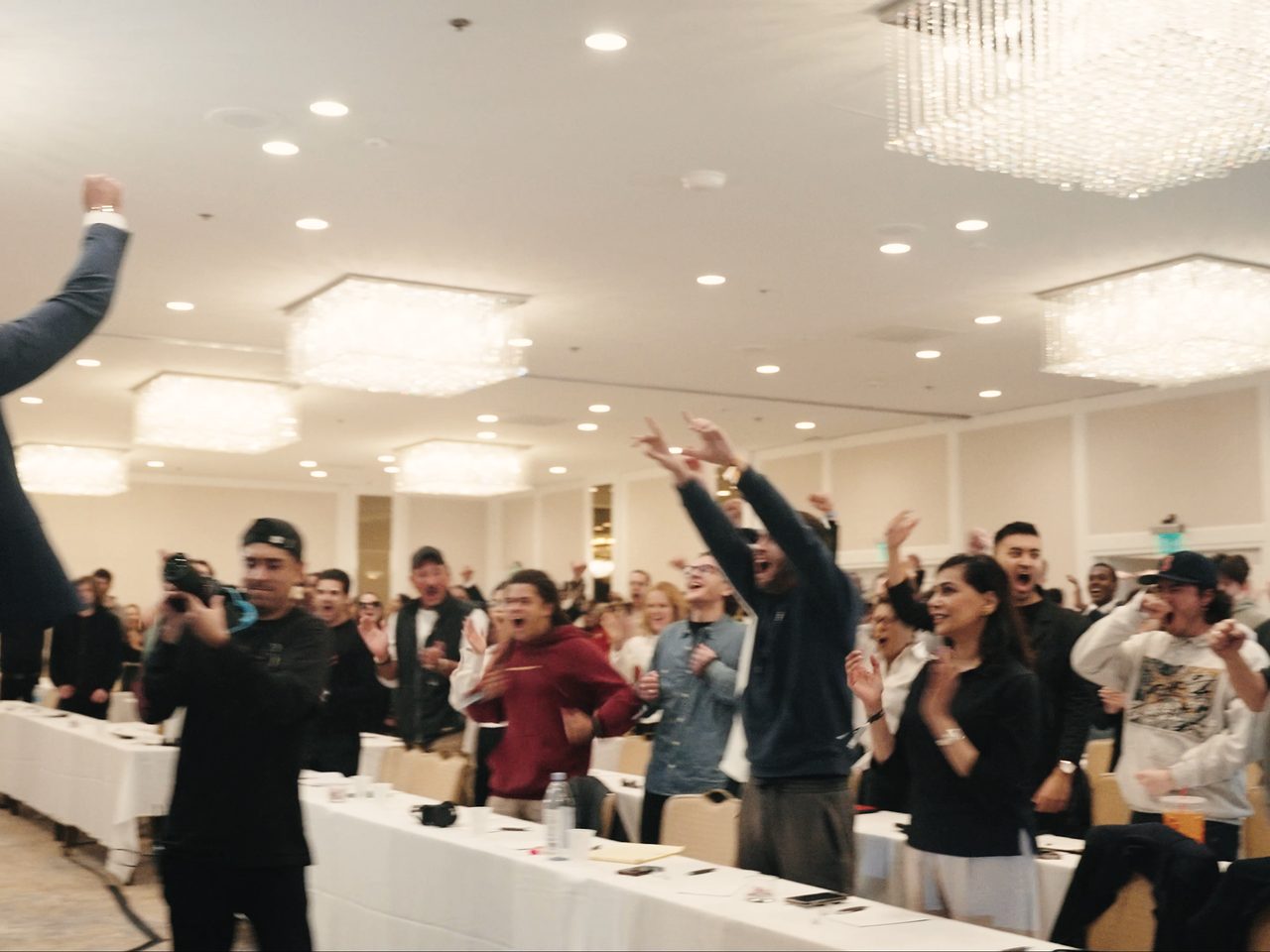 Marczell Klein, one arm raised, leading a ballroom of attendees on their feet.