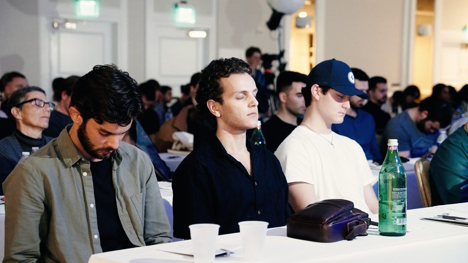 Seminar attendees seated at long tables, facing the stage.