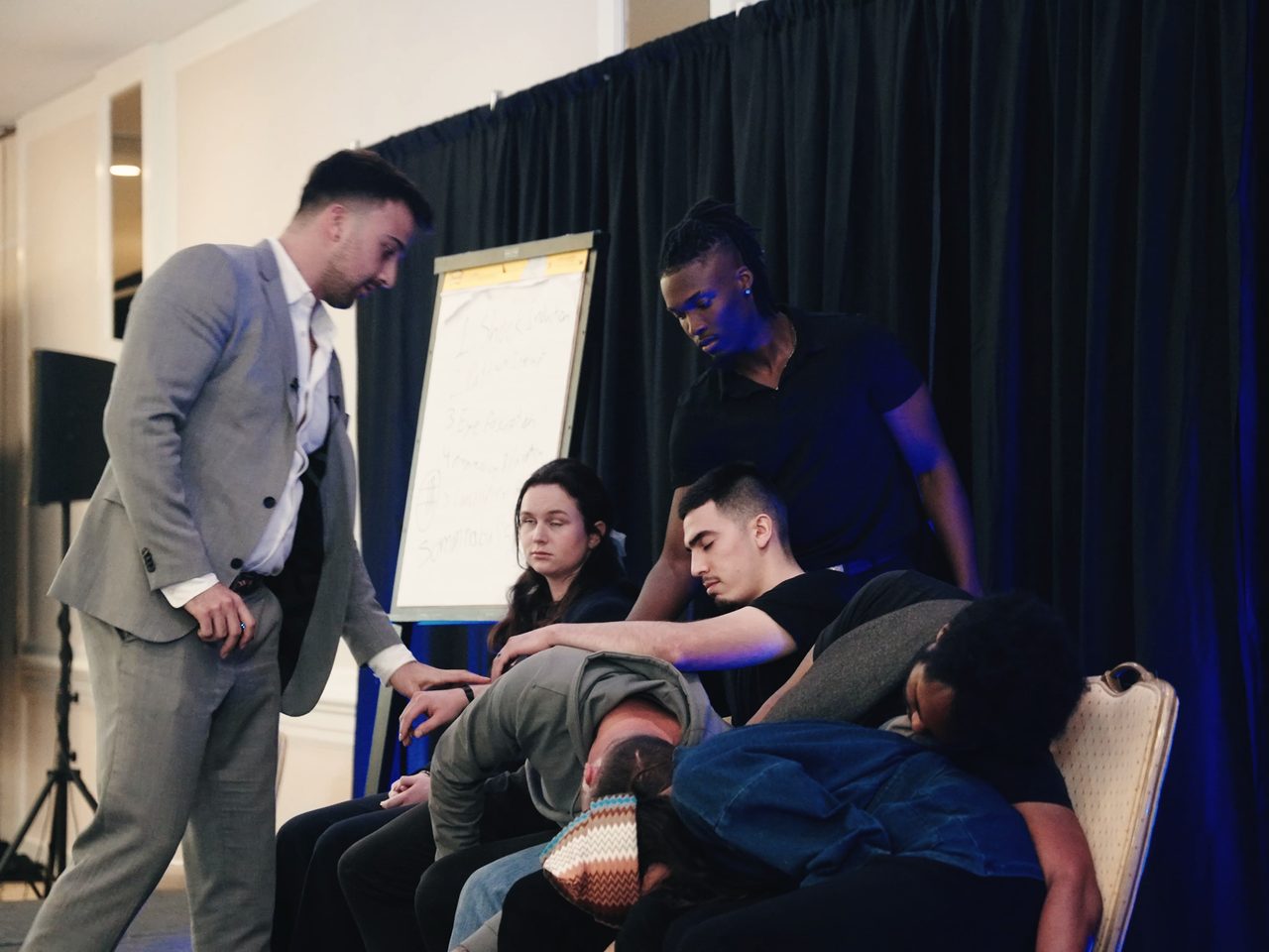 Participants lie on the stage floor during a guided hypnosis session while Marczell Klein walks past them.