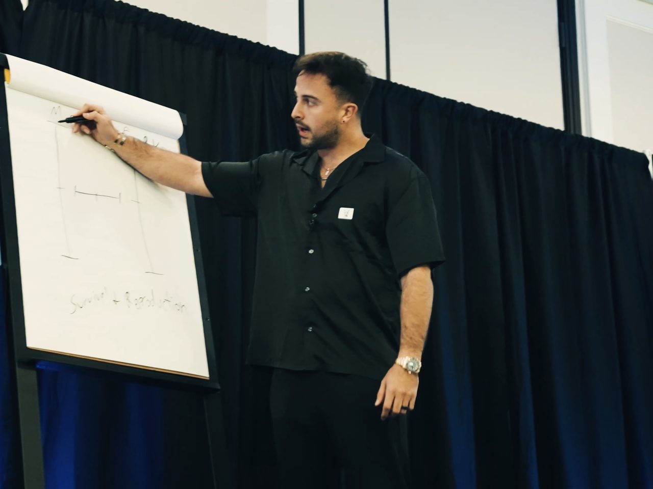 Marczell Klein writes on a flip chart in front of a dark blue curtain.