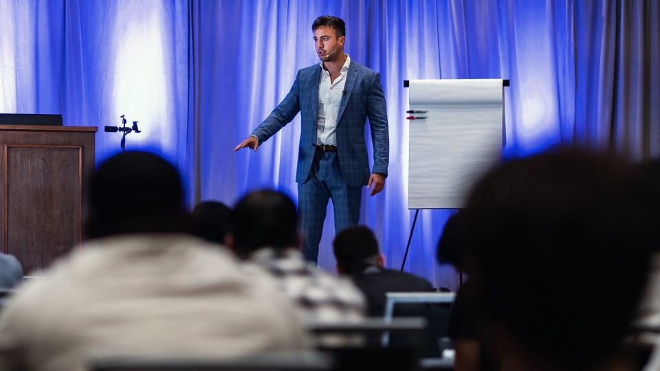 Marczell Klein on stage in a blue suit beside a flipchart, the audience in the foreground.