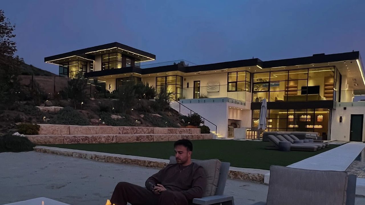 A modern hillside house at dusk, a long fire table burning on the terrace in front of it.