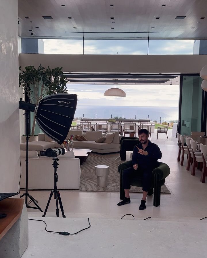 Marczell Klein seated in a bright living room, recording with a softbox light and a camera on a tripod.