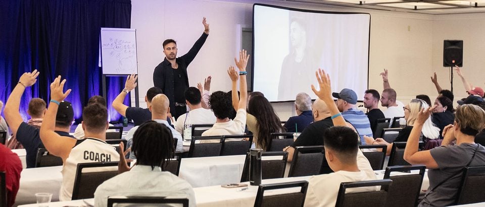A full seminar room, hands raised, seen from the back of the room.