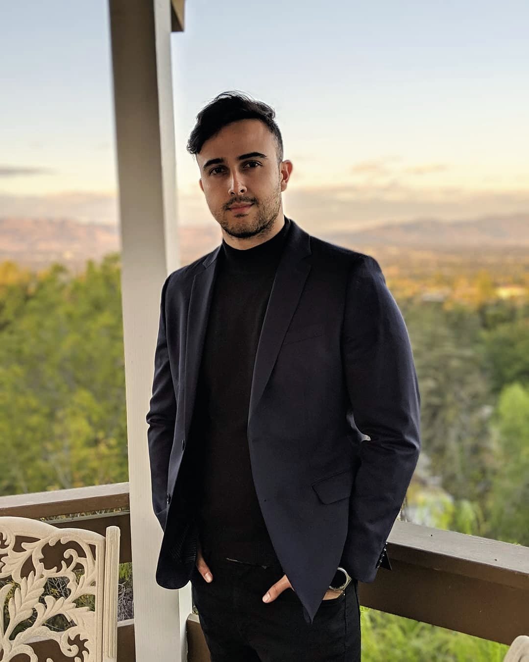 Marczell Klein in a dark blazer on a balcony at dusk, hills fading into the evening light behind him.